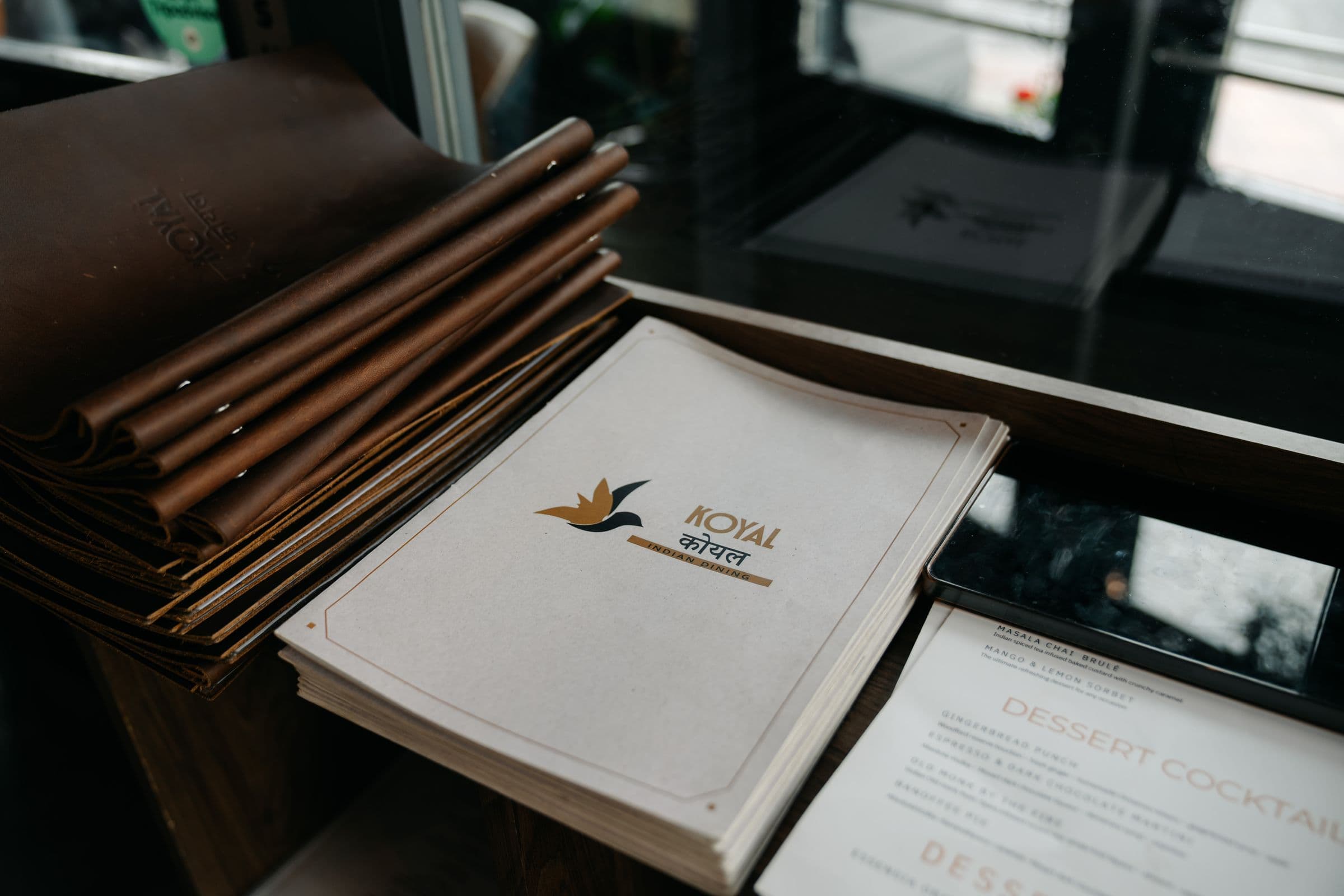 Leather-bound menu alongside beautifully presented dishes at Koyal Indian Restaurant